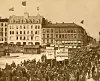 Dette bildet ble tatt på Youngstorget 1. mai 1908. I bakgrunnen ser vi det nye Folkets Hus. Parolene: 8 Timers Arbeidsdag - Arbeidere forener Eder - Bort med Overtidsarbeidet.