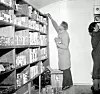 VARER: Melkekiosken ble Gjøvik og Vardal Samvirkelags avdeling på Vindingstad i 1956 med Oddvar Langerud og Sigrid Røstø bak disken. Her er de to i ferd med å fylle opp hyllene med det aller nødvendigste av matvarer. ↔