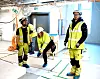 Jette Mari Øie tar på seg skoposer før vi går inn i et teknisk rom som er kommet såpass langt i byggeprosessen at det er behov for å ikke skitne til gulvet. T.v. Jan Nicholas Marin, t.h. Emil Thorainn Hardarson.