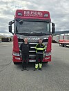 To menn foran en rød Scania-lastebil merket Gausdal Landhandleri på en gruslagt parkeringsplass.