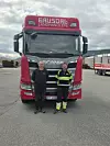 To menn foran en rød Scania-lastebil merket Gausdal Landhandleri på en gruslagt parkeringsplass.