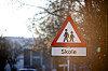 Skoleskilt med barnesymbol står foran trær.