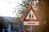 Skoleskilt med barnesymbol står foran trær.
