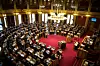 Oversiktsbilde av Stortingets sal med representanter, talerstol og rødt gulv.