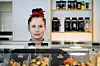 Astri Karine Lundgren bak en kantinedisk med matvarer, drikke og hyller i bakgrunnen.