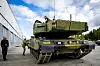 Grønn stridsvogn utenfor et verkstedbygg ved Rena leir, med personer i nærheten.