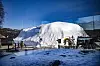 Snødekt område ved Snow Resort Kirkenes med en stor snøbygning og mørke trekonstruksjoner.