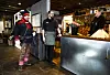 Tre personer i et rustikt serveringslokale, én i samisk bekledning og to bak en disk.