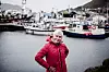 Guro Saniola Bjerk i rød jakke foran fiskebåter i havnen i Honningsvåg.