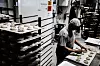 Baker arbeider med små bakverk på brett i et industribakeri.