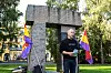 Jonas Bals står foran et steinmonument med fargerike flagg i en grønn park.