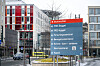 Blått og rødt veivisningsskilt ved St. Olavs hospital i Trondheim, omgitt av moderne sykehusbygg.