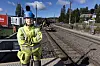 Banearbeider i verneklær står ved jernbanespor med tog og anleggsutstyr i bakgrunnen.