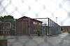 Inngjerdet område ved Hustad fengsel med murbygninger og våt asfalt i regnvær.