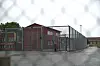 Inngjerdet område ved Hustad fengsel med murbygninger og våt asfalt i regnvær.