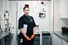 Astri Karine Lundgren i mørk arbeidsuniform og oransje hansker i et industrielt kjøkkenmiljø.