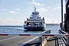 Bastøferga nærmer seg kaia i Horten, sett fra en rampe med sjøen og bryggeanlegg rundt.