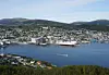 Illustrert flyfoto av Harstad havn med tett boligbebyggelse, fjord, planlagt hall og skogkledde åser.