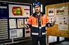 Person i verneklær står mellom informasjonstavler med tekst og illustrasjoner.
