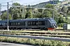 Et moderne grått og grønt fjerntog kjører langs jernbanespor i et kupert landskap.