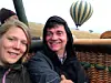 En mann og en kvinne smiler fra kurven på en luftballong, mens en ballong svever over landskapet i bakgrunnen.