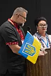 Oleg Grygoriuk taler i mikrofon ved siden av Antonina Shkamerda med Ukrainas flagg i forgrunnen.