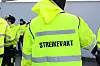 Person i gul refleksvest merket «STREIKEVAKT», omgitt av andre streikevakter.