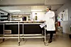 Person i hvit arbeidsfrakk og hårnett står ved en tralle i et industrikjøkken.