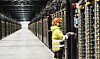 Tekniker i verneklær arbeider ved serverrack i en lang datasenterhall.
