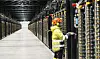 Tekniker i verneklær arbeider ved serverrack i en lang datasenterhall.