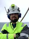 Arbeider i grønn synlighetsjakke og verneutstyr står foran havet.