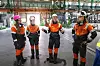 Fire arbeidere i verneutstyr snakker sammen i et stort industrilokale.