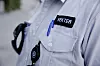 Nærbilde av lys vekteruniform med merket «VEKTER» og kontrollutstyr.