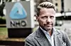 Kjetil Staalesen i grå blazer foran et skilt med NHO-logoen.
