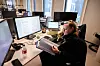 Linda Hægdahl sitter ved en kontorpult med flere skjermer og holder et dokument.