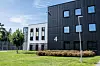 Fengselsbygning med mørk fasade og tallet 4, omgitt av plen, trær og sikringsgjerde.