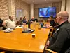 Møte med flere deltakere rundt et bord på Stortinget, med en presentasjonsskjerm i bakgrunnen.