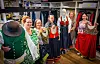 En gruppe ansatte i tradisjonelle drakter står sammen i systua med klær og utstyr rundt seg.