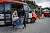 Bussjåfør hjelper en eldre kvinne med en trillevogn ved en åpen Skyss-buss i Solund.