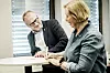 Raymond Johansen og Anne Berit Aker Hansen signerer dokumenter ved et skrivebord på et lyst kontor.