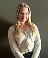 Portrett av Victoria Innerdal i lys strikket cardigan foran en mørk vegg.