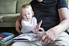 Barn og pappa ser i en illustrert bok sammen i en sofa, med flere bøker på bordet.