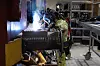 Verkstedarbeider i verneutstyr sveiser på en stor metallkomponent i et togverksted.