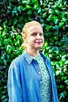 Eva Seth i dongerijakke foran en frodig, grønn hekk.