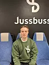 Jacob Anker Eide sitter i et blått bussete foran Jussbuss-logoen.