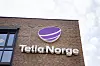 Telia Norge-logo på en rødbrun mursteinsbygning under en lys himmel.
