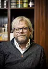 Portrett av Torfinn Håverstad med briller og mørk genser foran hyller i et innendørs miljø.