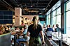 Servitør sett bakfra beveger seg mellom gjester i en lys, moderne restaurant.