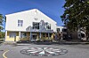 Lys skolebygning med trær, vinduer og et fargerikt sirkelmotiv på bakken foran.