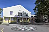Lys skolebygning med trær, vinduer og et fargerikt sirkelmotiv på bakken foran.